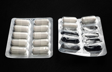 Medicine. White capsule pills in two, whole and open blister packs on a black background....