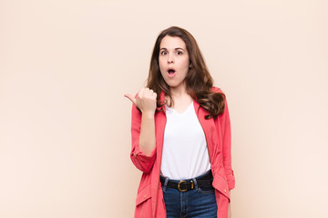 young pretty woman looking astonished in disbelief, pointing at object on the side and saying wow,...