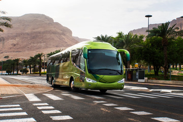 Passenger tourist bus rides on an asphalt road against background of mountains and palm trees.