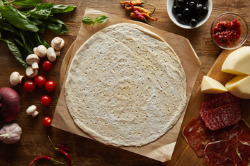 Top view of raw dough with ingredients for pizza on wooden table