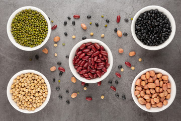 Grains or beans, red bean, black bean, green bean, soybean, peanut in the white bowl placed on the black cement floor. Top view.