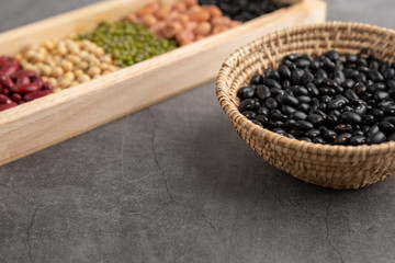 Black beans and grains in the wooden basket and in the wooden tray placed on the black cement floor. High angle view.