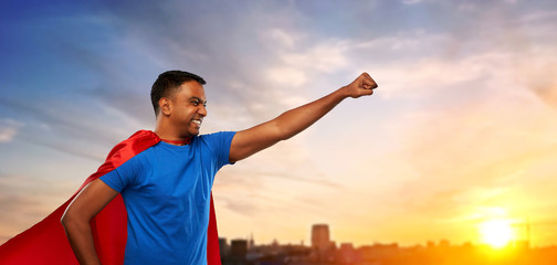 Fototapeta na wymiar super power and people concept - indian man in red superhero cape making winning gesture over sunset in city background
