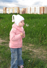 Little girl in knitted hat blowing on white dandelion.