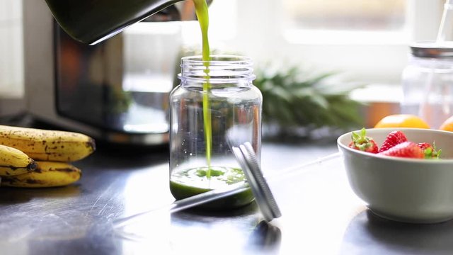 Green juice is poured into a jam jar