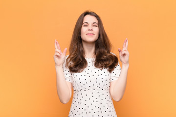 young pretty woman smiling and anxiously crossing both fingers, feeling worried and wishing or...