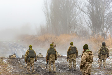 Privates and officers in camouflage and body armor shoot Kalashnikovs at targets in the shooting...