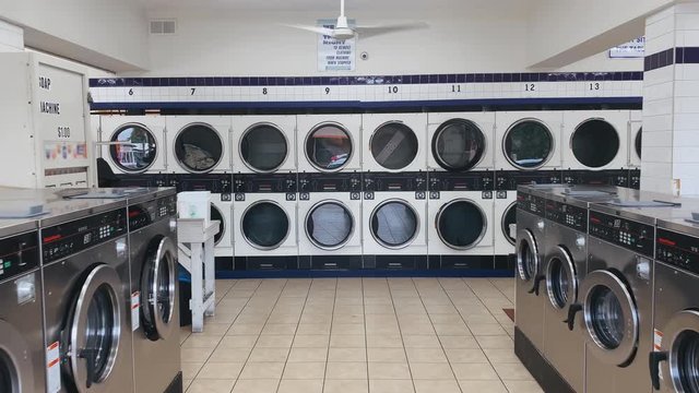 Interior of large self service laundry shop with ceiling fan. Rows and lines of working washing machines and tumble dryers. Electricity consumption
