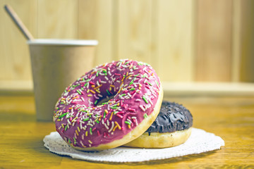 Paper cup of coffee and donut with icing on a wooden table. The concept of a quick breakfast, snack.