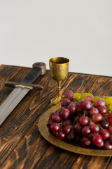 ancient cup, sword and grape on wooden table isolated on grey