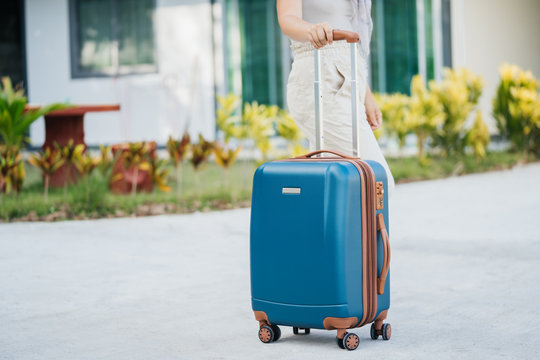 tourist blue suitcase is held by a female hand on a background of a tropical house. time to travel and vacation.