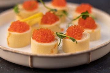 Dough rolls with cheese, red caviar. Garnished with sprigs of microgreen, a slice of lemon. On a wooden natural background.