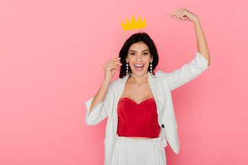 smiling woman pointing with finger at paper crown on pink background