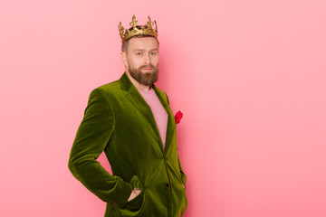 handsome man with crown in velour jacket looking at camera on pink background