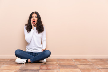 Young woman sitting on the floor surprised and shocked while looking right