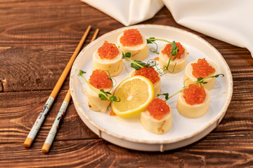 Dough rolls with cheese, red caviar. Garnished with sprigs of microgreen, a slice of lemon. On a wooden natural background.