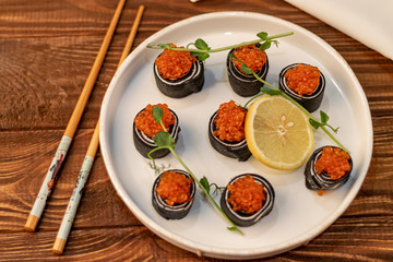 Dough rolls with cheese, red caviar. Garnished with sprigs of microgreen, a slice of lemon. On a wooden natural background.