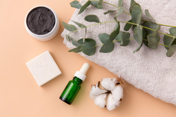 Fototapeta na wymiar beauty and spa concept - serum or essential oil, mask, soap bar, eucalyptus cinerea and cotton flower on bath towel