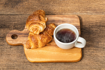 A white cup of hot coffee with croissant on wooden background.