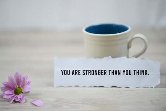 Inspirational quote - You are stronger than you think. With a cup of morning coffee and beautiful purple daisy flower on white wooden table background. Motivational words on paper note concept.