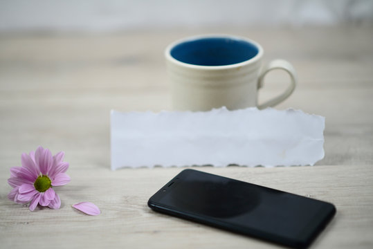Empty cup with blank torn paper, purple flower and black phone on white table background. Still life concept with copy space for inspirational or motivational text design. - Powered by Adobe
