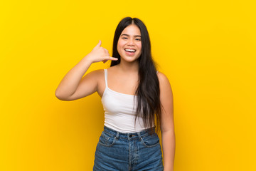 Young teenager Asian girl over isolated yellow background making phone gesture. Call me back sign