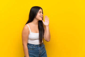 Young teenager Asian girl over isolated yellow background shouting with mouth wide open to the lateral