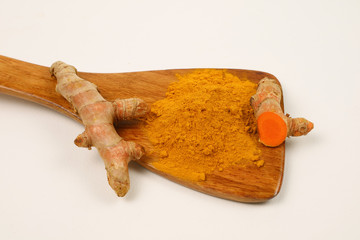 Turmeric powder in a wooden spoon and turmeric root extracted on a white background, used as a tonic for the body and food ingredients.