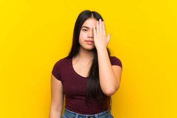 Young teenager Asian girl over isolated yellow background covering a eye by hand