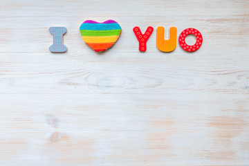 Inscription I love you written in wooden made letters and rainbow heart-shaped pillow on wood vintage background