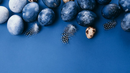 Beautiful group ombre blue Easter eggs with quail eggs and feathers on a blue background. Easter concept. Border eggs. Copy space for text