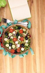 Authentic fresh salad in a stone cup with dumbbells excercise equipment, measuring tape on table. healthy lifestyles, good health Concept with fresh ingredients