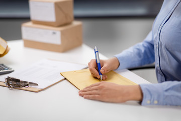 delivery, mail service, people and shipment concept - close up of woman with pen writing address on...