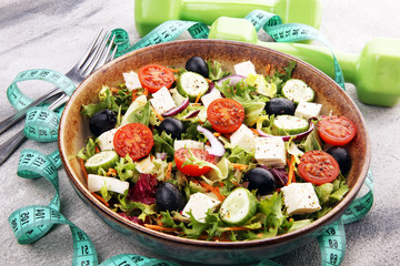 Authentic fresh salad in a stone cup with dumbbells excercise equipment, measuring tape on table. healthy lifestyles, good health Concept with fresh ingredients