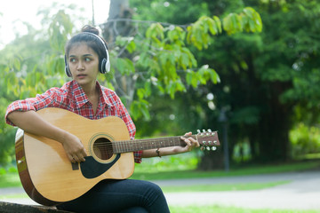 asian girls wear knit hats and listen to music through earphones, ready to play guitar in the morning garden of the holidays