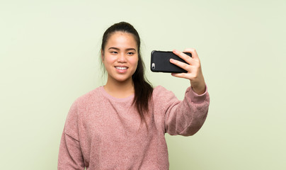 Young teenager Asian girl over isolated green background making selfie with cellphone