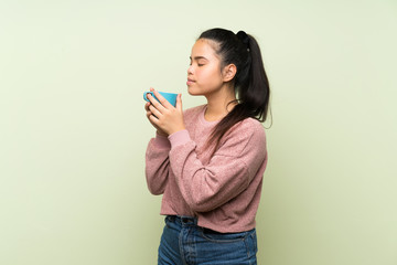 Young teenager Asian girl over isolated green background holding hot cup of coffee