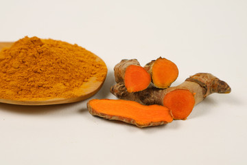 Turmeric powder in a wooden spoon and turmeric root extracted on a white background, used as a tonic for the body and food ingredients.