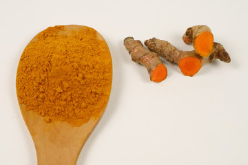 Turmeric powder in a wooden spoon and turmeric root extracted on a white background, used as a...