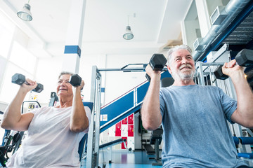 couple of seiors and pensioner at the gym doing exercise together  - man and woman holding...