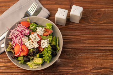 Greek vegetable salad. It consists of tomatoes, olives, feta cheese, herbs, cucumbers and red onions. On a wooden background.