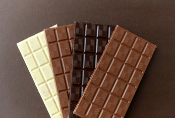 sweets, confectionery and food concept - milk, dark and white chocolate bars on brown background