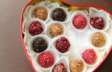 sweets, confectionery and food concept - candies in red heart shaped chocolate box on brown background