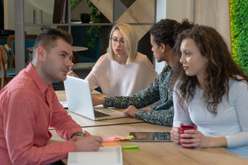 University students sitting together at table with books and laptop.