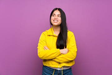 Young teenager Asian girl over isolated purple background looking up while smiling