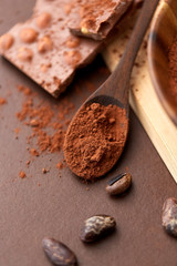 sweets, confectionery and culinary concept - cocoa powder in wooden spoon with chocolate and beans on brown background