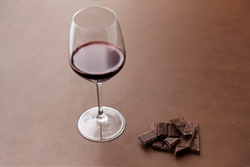 dessert concept - dark chocolate pieces and glass of red wine on brown background