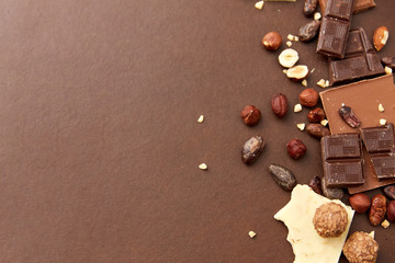 sweets, confectionery and food concept - milk, dark and white chocolate bars with hazelnuts and...