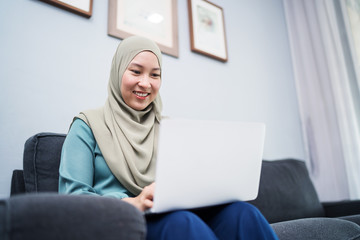 Female muslim using laptop at home environment.
