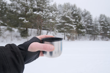 cup with hot tea in hand on a forest background first-person view